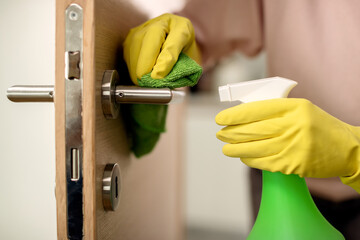 Cloe-up of woman disinfecting door handle at home.