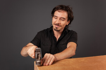 A man hammers nails into a cupboard. The back wall of the cupboard is made of thick cardboard.