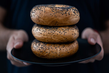 A men's hands holding a plate full of Bagels on a Black Background