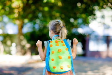 Naklejka premium Cute little adorable toddler girl on her first day going to playschool. Healthy beautiful baby walking to nursery preschool and kindergarten. Happy child with backpack on the city street, outdoors.