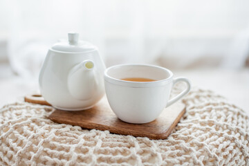 A mug of hot tea, a teapot, a wooden stand on an ottoman. Cozy autumn. Winter breakfast. Cotton.
