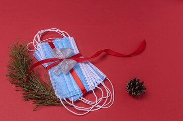 medical protective face masks tied with a red gift ribbon, a Christmas pine branch and a cone on a red background