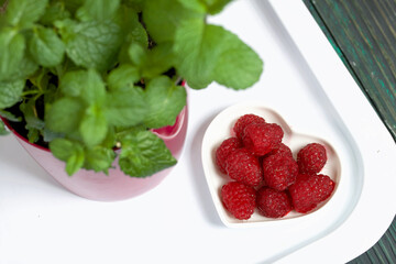 Raspberries on a white surface. Nearby is a pot of mint. On the surface of pine boards painted in black and green.
