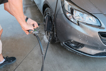 Man washing car's wheel with a special brush close-up. Car wash service/business. Transportation.