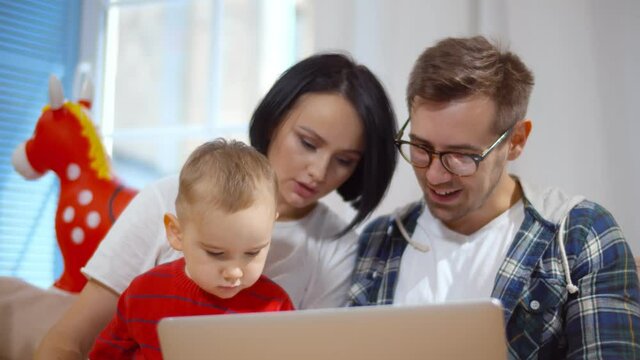 Young parents watching cartoons on laptop with cute baby boy