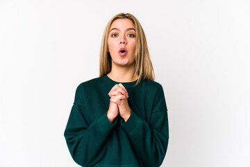 Young blonde caucasian woman isolated praying for luck, amazed and opening mouth looking to front.