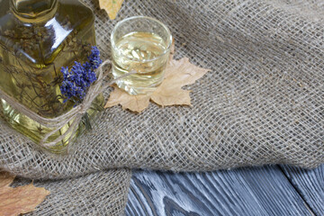 A bottle of lavender tincture. A bouquet of lavender is tied to the bottle. Nearby is a glass of drink and dried maple leaves. On coarse linen. Close-up shot.