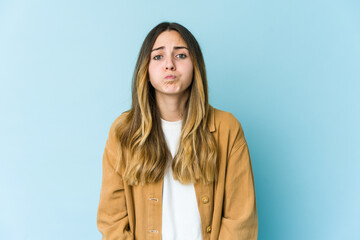 Obraz premium Young caucasian woman isolated on blue background blows cheeks, has tired expression. Facial expression concept.