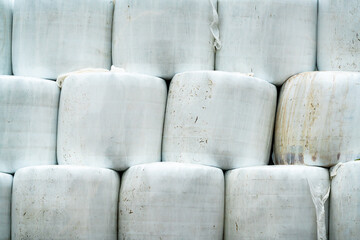 Silage hay bales wrapped in white plastic, stacked on top of each other.