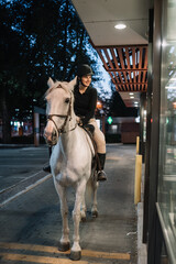 a young woman on a white horse smiling stands near an establishment with food and fast food and...