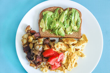 Balanced healthy vegetarian breakfast avocado toast, scrambled eggs, potatoes and tomato.