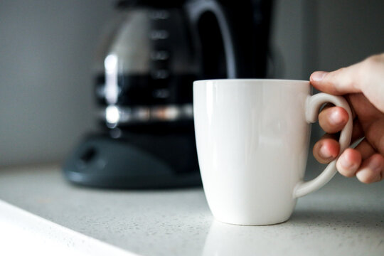 Holding white coffee cup in front of coffee maker