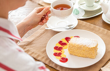 girl drinking tea with cake napoleon. a slice of napoleon cake on a white plate on a served table. In the background there is a kettle, tea, juice.