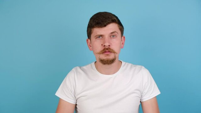 Portrait of young man showing stupid gesture and pointing to camera, accusing crazy cuckoo mind, reckless plan, blaming insane idea, wears white t-shirt, isolated on pastel blue studio background