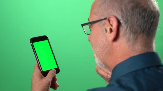 Green screen background with tablet also having green screen of man talking to someone over video call on his phone and smiling and laughing.