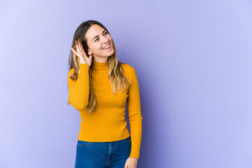 Young caucasian woman isolated on purple background trying to listening a gossip.