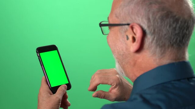 Green screen background with tablet also having green screen of man talking to someone over video call on his phone and smiling and laughing.