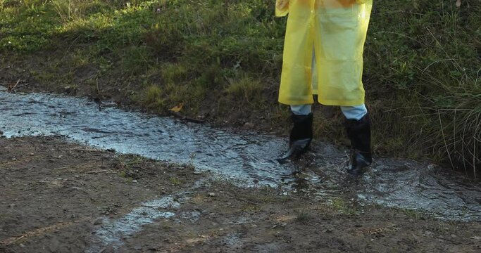 woman in a yellow raincoat and rubber boots jumping through puddles