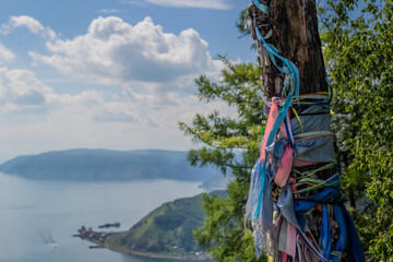 multicolored ribbons on a tree trunk against the backdrop of a landscape of blue lake baikal among green mountains