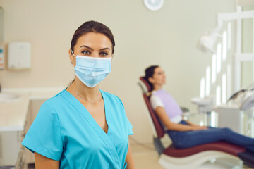 Woman doctor dentist in medical uniform and mask standing and looking at camera in clinic
