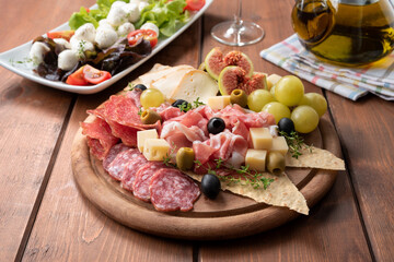 Tipico tagliere di antipasti misti con prosciutto crudo, salame, formaggi, olive e frutta fresca,...