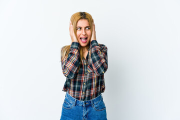 Young blonde woman isolated on white background covering ears with hands trying not to hear too loud sound.