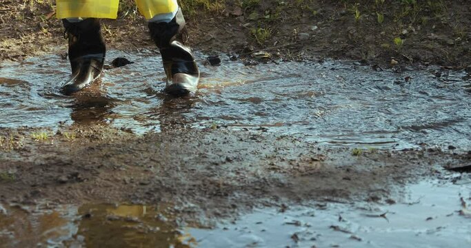 woman in a yellow raincoat and rubber boots jumping through puddles