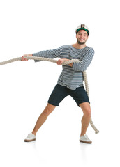 Pulls the rope, tug of war. Caucasian male sailor in uniform on white studio background. Young man using modern devices and gadgets. Concept of tech, professional occupation, job of seaman, emotions.
