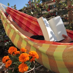 A person relaxing in colorful hammock and enjoying a book in a garden in a sunny day.  Selective...