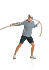 Pulls the rope, tug of war. Caucasian male sailor in uniform on white studio background. Young man using modern devices and gadgets. Concept of tech, professional occupation, job of seaman, emotions.