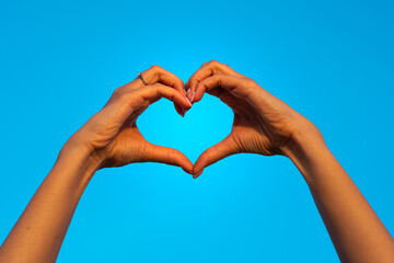 Fototapeta premium Young woman hands making heart shape symbol of love isolated on blue sky. Girl falls in love. Valentine card ideas
