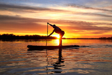 Silhouette of woman paddle on stand up paddle boarding (SUP) on quiet winter or autumn river at...