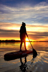 Silhouette of woman paddle on SUP (stand up paddle board) on quiet river at dusk. Winter sport