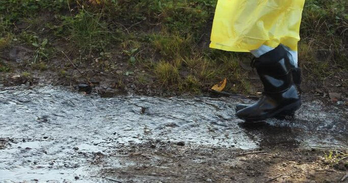 woman in a yellow raincoat and rubber boots jumping through puddles