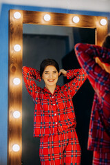 Pretty woman in red pajamas standing near a mirror looking at her reflection