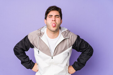 Young man isolated on purple background funny and friendly sticking out tongue.