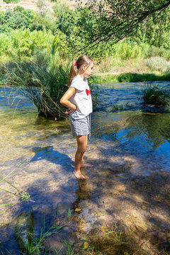 Pretty little girl in a white t-shirt wetting her feet in the cool waters of the Mijares River