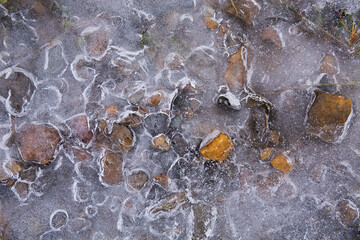 Obraz premium A thin layer of ice mostly covers colorful, small stones 