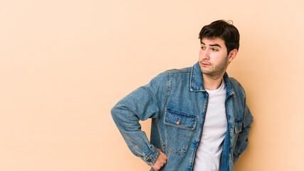 Young man isolated on beige background looks aside smiling, cheerful and pleasant.