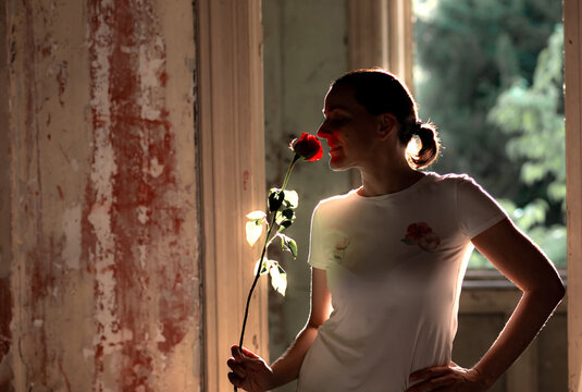 Silhouette of a young woman smelling a red rose in a ruined, abandoned house. Happiness. Bad times - good times concept. Backlight.