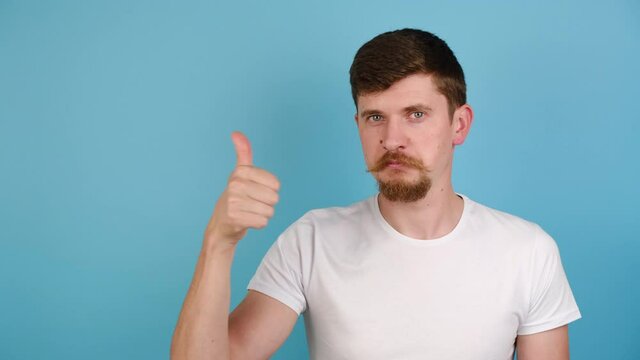 Young man showing okay hand sign and winking as if approving suggestion, millennial guy completely agree and support, dressed in white t-shirt, isolated on blue studio background with copy space
