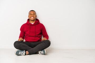 Young latin man sitting on the floor isolated laughs and closes eyes, feels relaxed and happy.