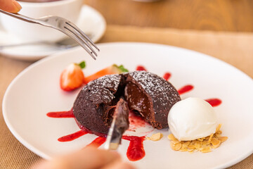 The girl cuts the chocolate fondant with a knife. Chocolate dessert, plate decorated with jam and strawberry wedge.