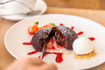 The girl cuts the chocolate fondant with a knife. Chocolate dessert, plate decorated with jam and strawberry wedge.