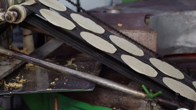 Closeup view of tortillas stamped out into perfect circles move down a conveyor belt towards the oven where they are cooked.