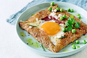 Breton traditional pancake made from buckwheat flour with ham, cheese, egg, feta, green peas and green butter. Breakfast of buckwheat thin pancakes with fried eggs, ham and cheese, eggs for breakfast