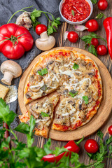 Homemade pizza with tomatoes, mushrooms and green basil.