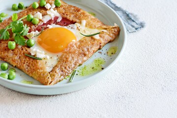 Breton traditional pancake made from buckwheat flour with ham, cheese, egg, feta, green peas and green butter. Breakfast of buckwheat thin pancakes with fried eggs, ham and cheese, eggs for breakfast