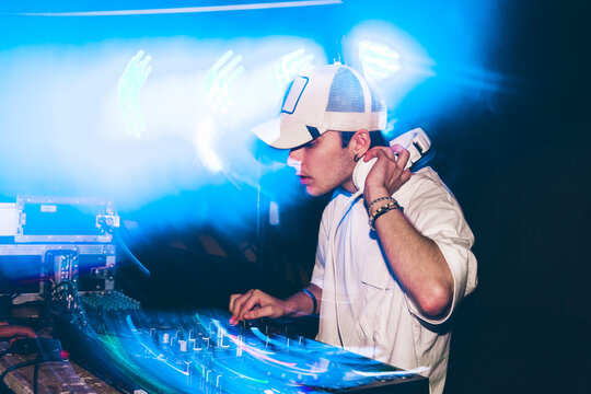 DJ with headphones at night club party under the blue light and people crowd in background