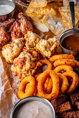 beer plate with spicy chicken wings, chips, fries onion rings, cheese balls, breaded, tartar sauce on wooden table
